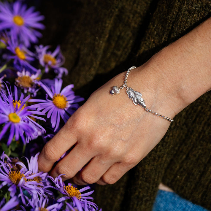 Hand wearing a silver bracelet with leaf charm holding purple flowers