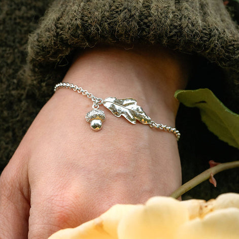 Hand wearing a silver bracelet with a yellow rose and green leaves in the background