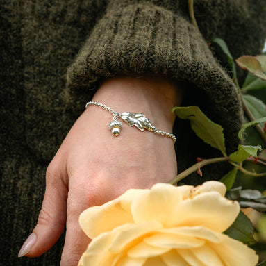Hand wearing a silver bracelet with a yellow rose and green leaves in the background