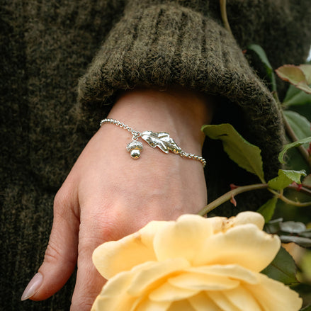 Hand wearing a silver bracelet with a yellow rose and green leaves in the background