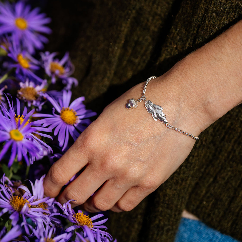 Hand wearing a silver bracelet with leaf charm holding purple flowers