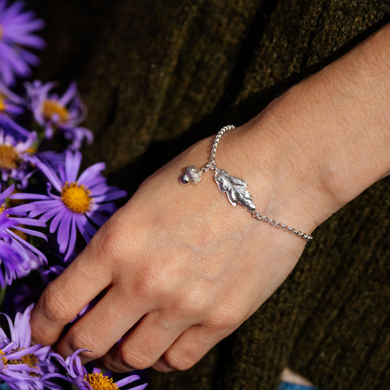 Hand wearing a silver bracelet with leaf charm holding purple flowers