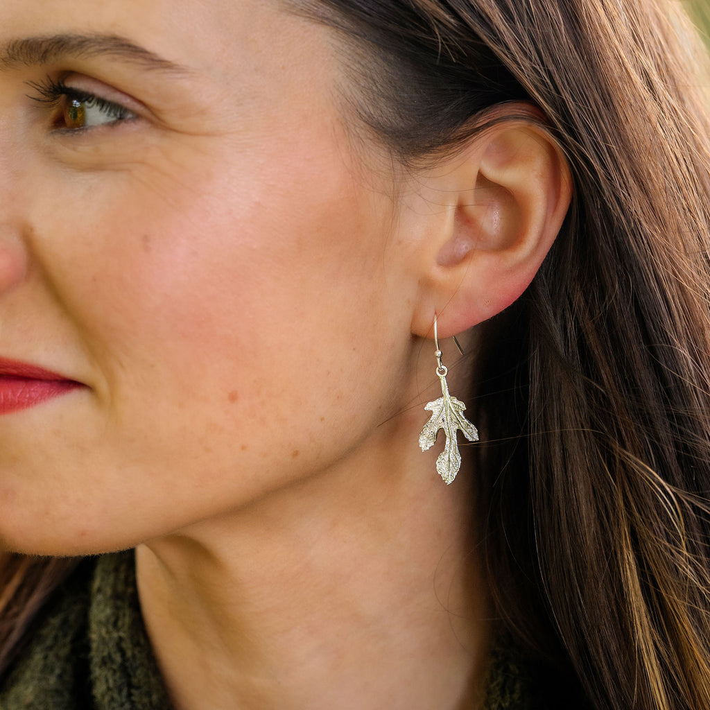 Close-up of a woman wearing a silver fig leaf-shaped earring.