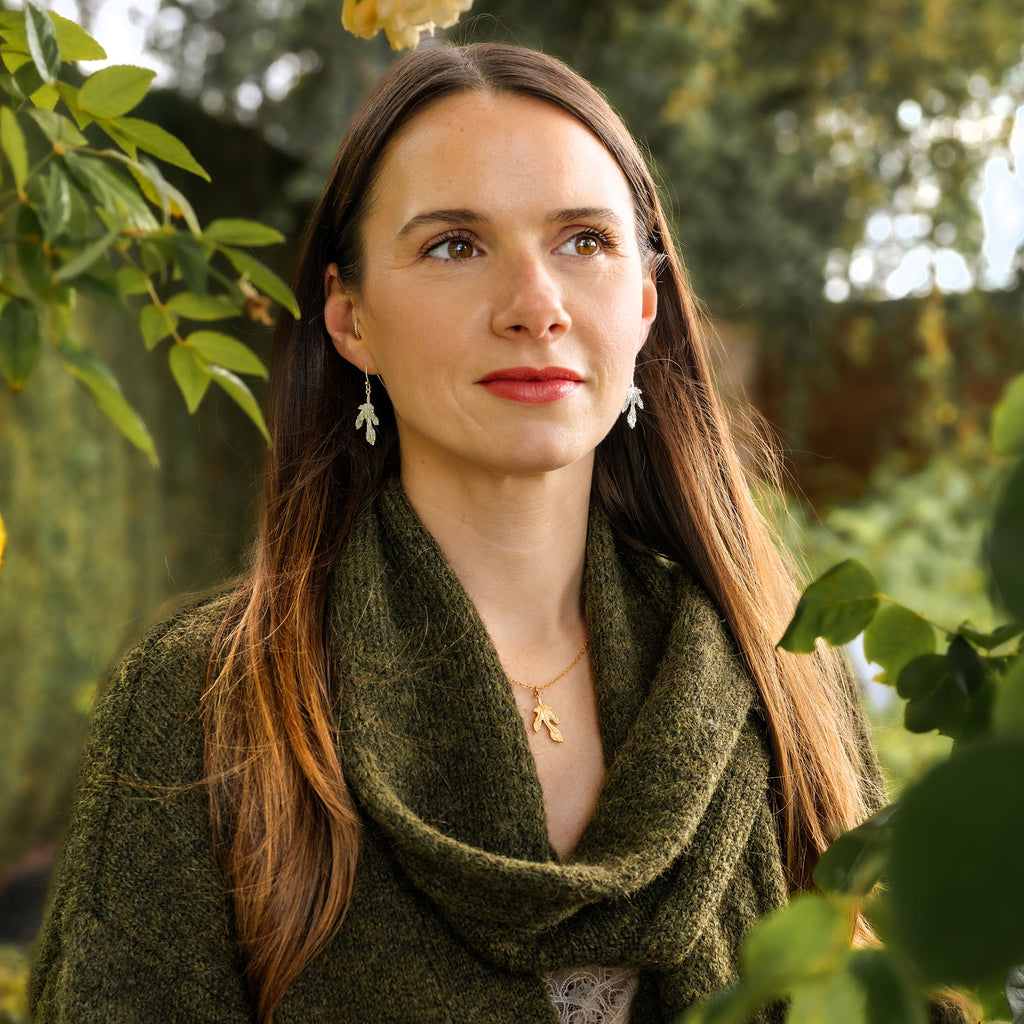 Woman wearing a green scarf in a natural setting with trees and foliage.