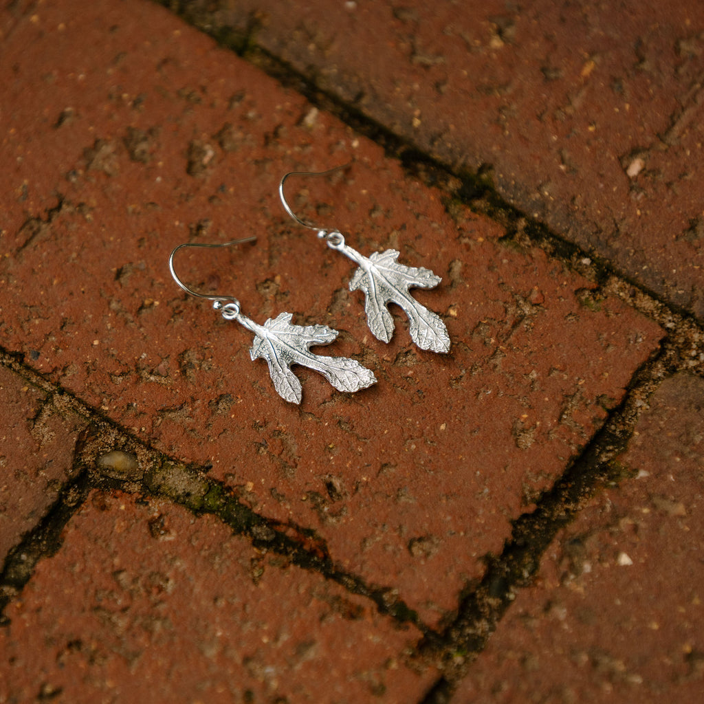 Silver fig leaf-shaped earrings on a brick surface