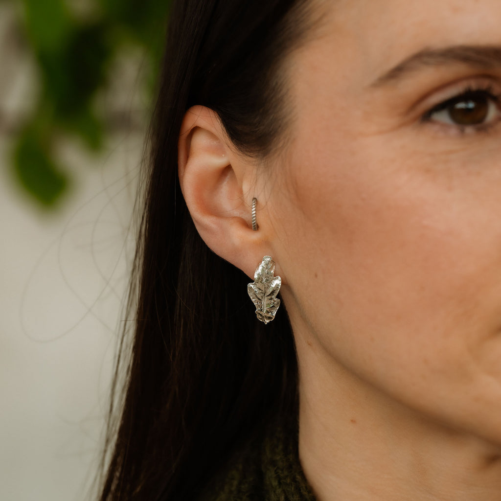 Close-up of a woman wearing silver Oak leaf-shaped earrings with a blurred background