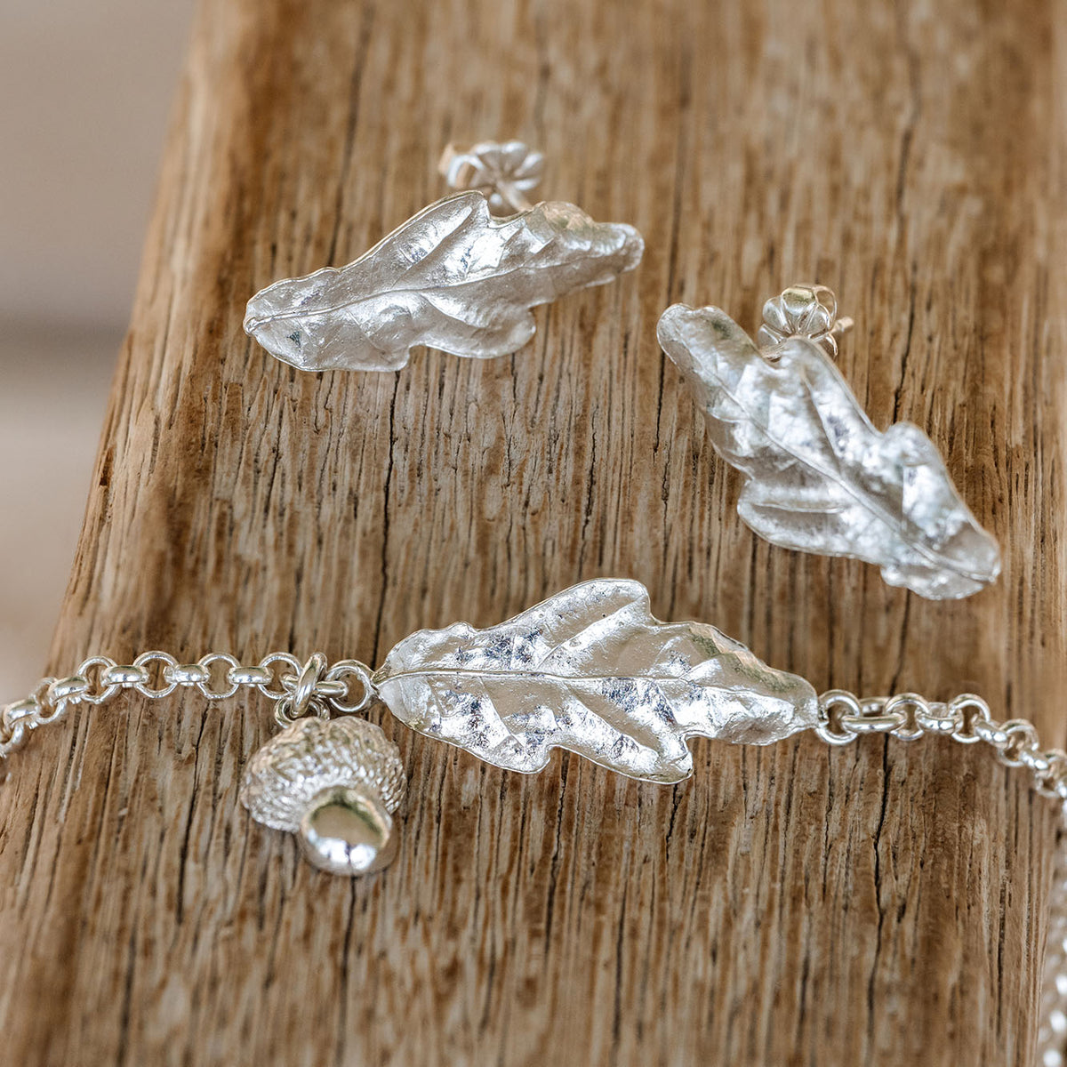Silver Oak leaf-shaped jewelry set on a wooden surface