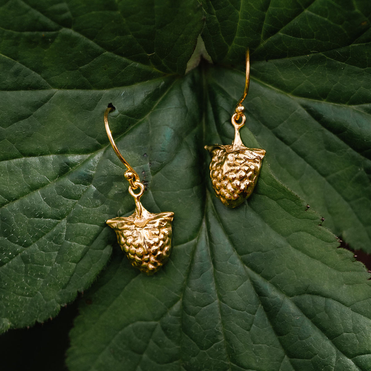 Gold raspberry shaped earrings on a green leaf