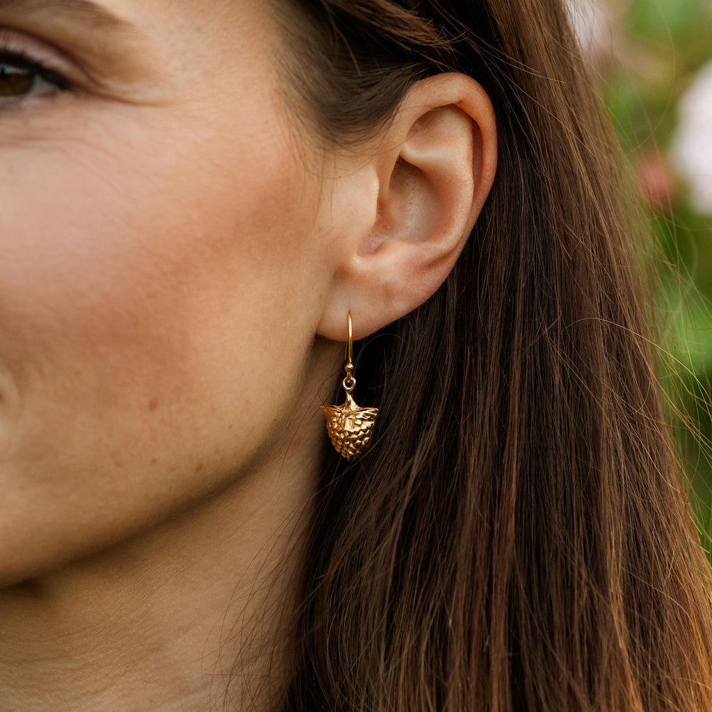 Close-up of a woman wearing a gold earring with a raspberry design.